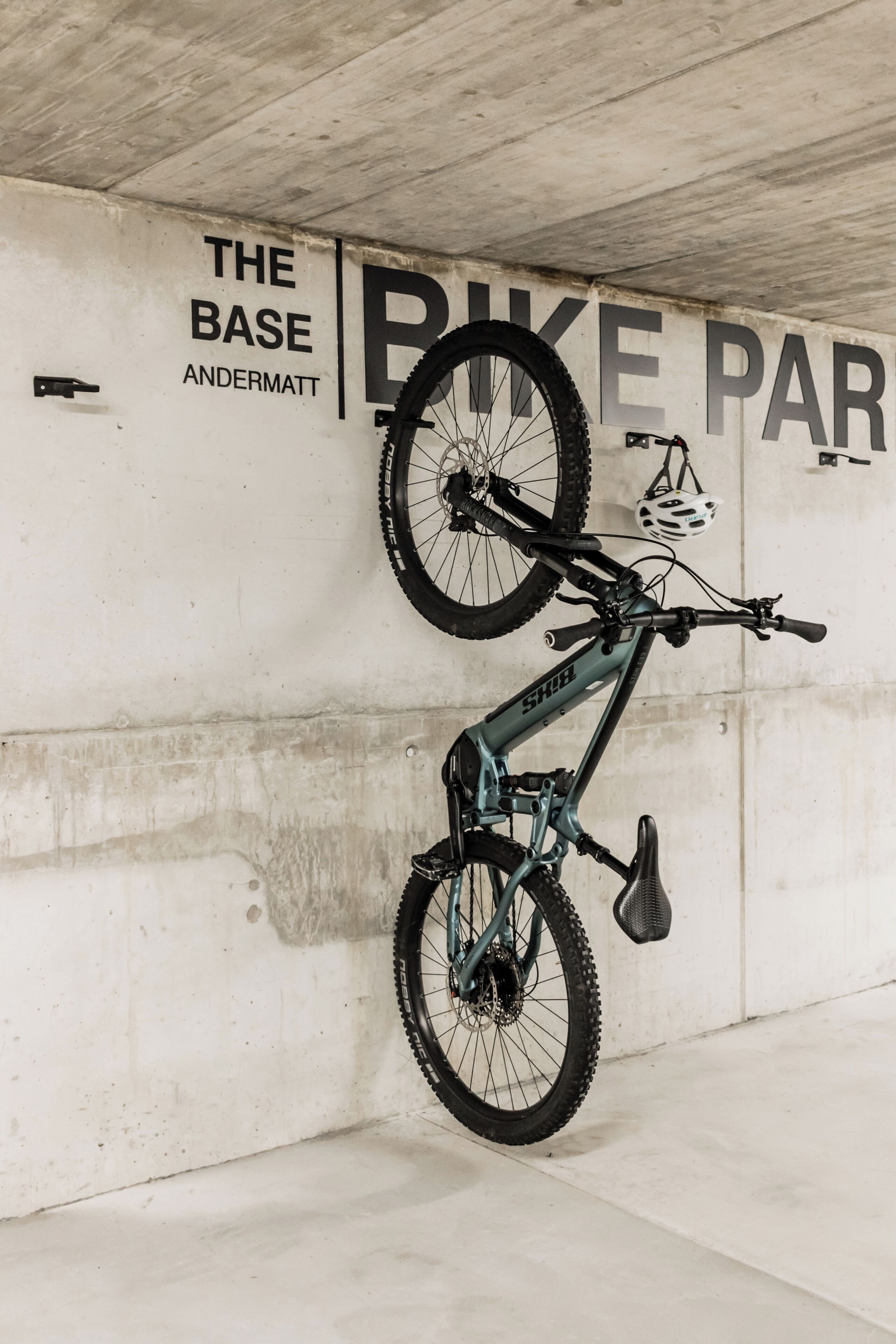 A bicycle parked in a garage with a wall that reads 'THE BASE ANDERMATT BIKE PARK.'