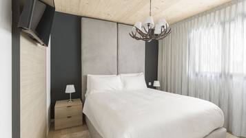A modern bedroom with a large bed, a nightstand, a TV mounted on the wall, and a chandelier.