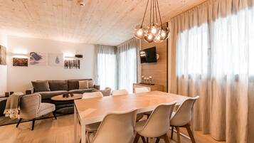 Una sala moderna con techo de madera, una mesa de comedor con sillas, un sofá y un televisor montado en la pared.
