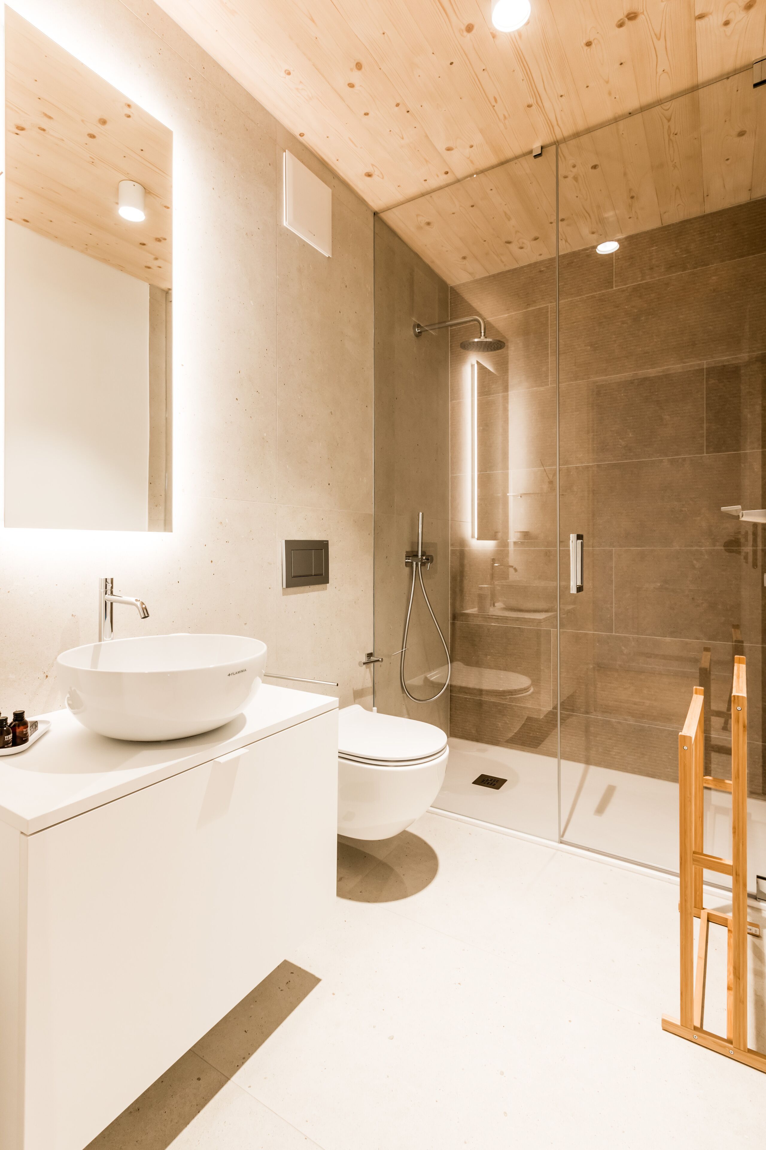 A modern bathroom with a large white sink, a glass shower enclosure, and a wooden ladder.