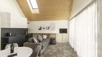Ein modernes Wohnzimmer mit grauem Sofa, einem runden Couchtisch und einem Fernseher an der Wand.