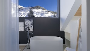 A modern bathroom with a freestanding bathtub, a large window offering a mountain view, and a minimalist design. - THE BASE  (Andermatt)