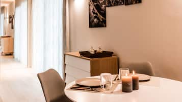 Un coin repas avec une table dressée pour deux personnes, des bougies et un plateau avec des verres, le tout posé sur un buffet en bois.