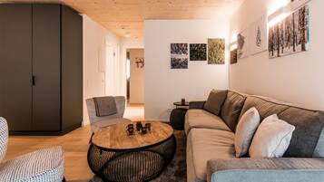 Ett modernt vardagsrum med ett träpanelat tak, en grå soffa, en mönstrad fåtölj, ett runt soffbord och konstverk som hänger på väggen.