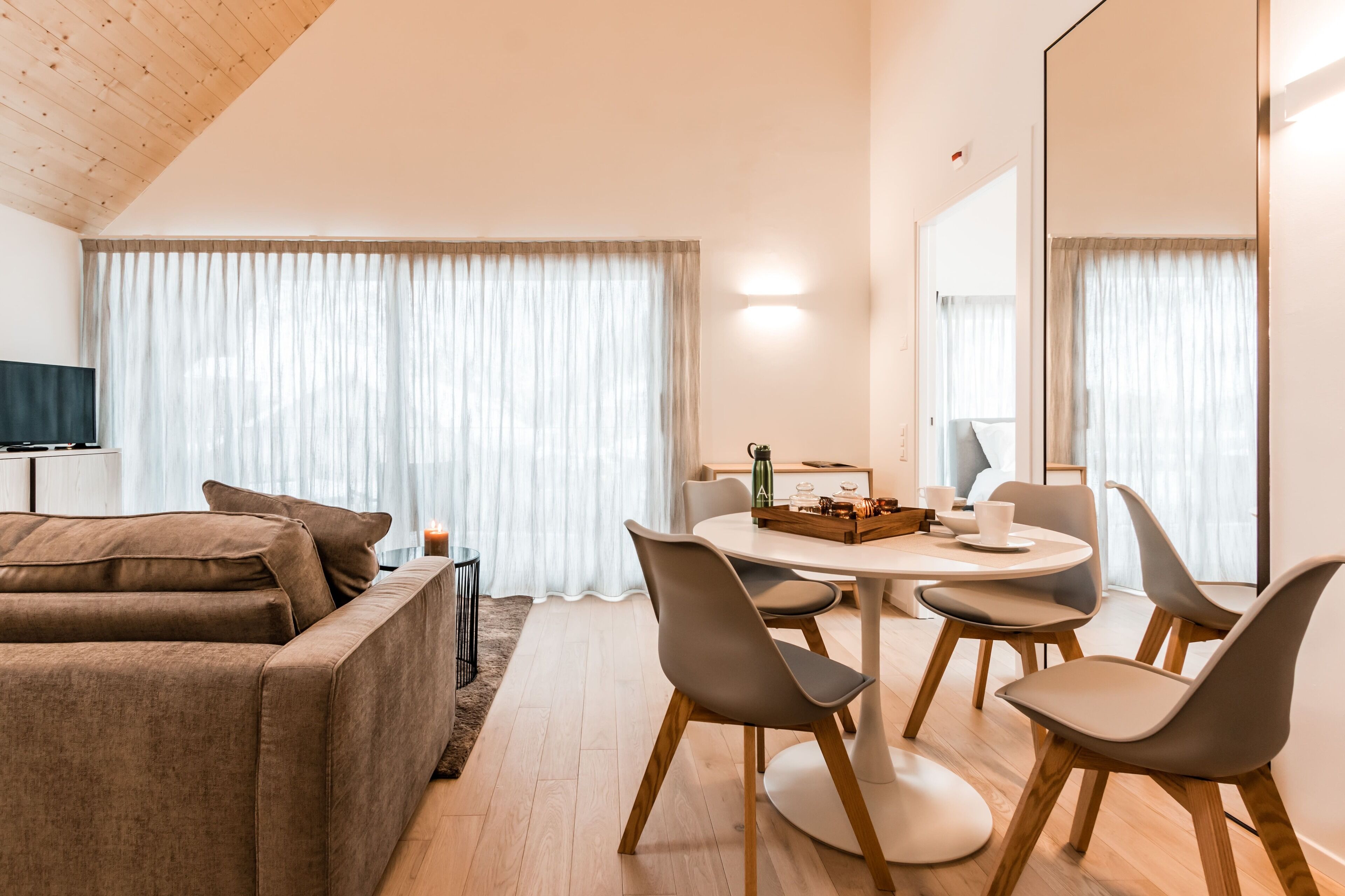 Un salon moderne avec un canapé, une table à manger et des chaises, ainsi qu’une grande fenêtre avec des rideaux.