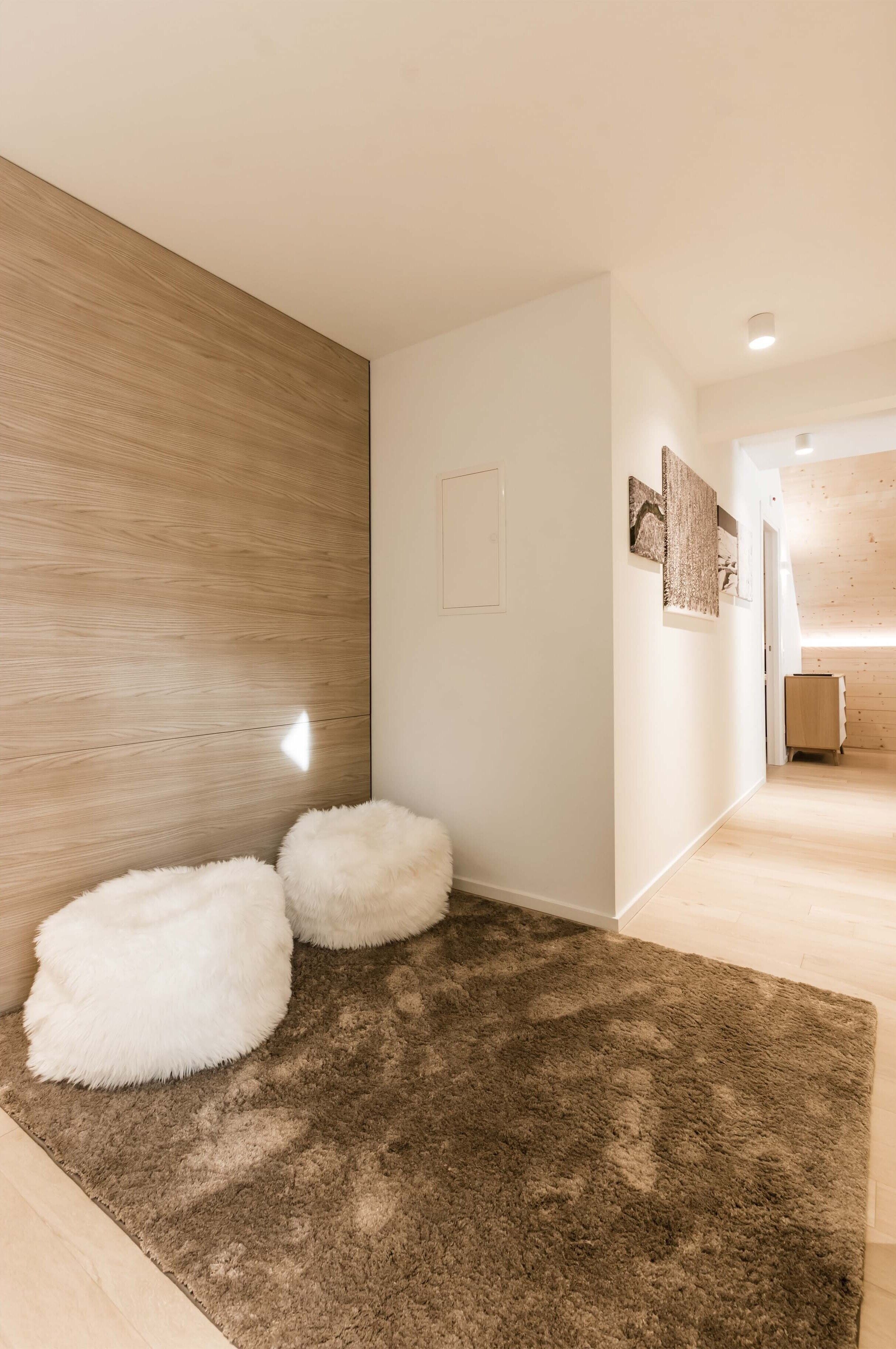 A hallway with a wooden accent wall, a brown rug, and two fluffy white poufs.