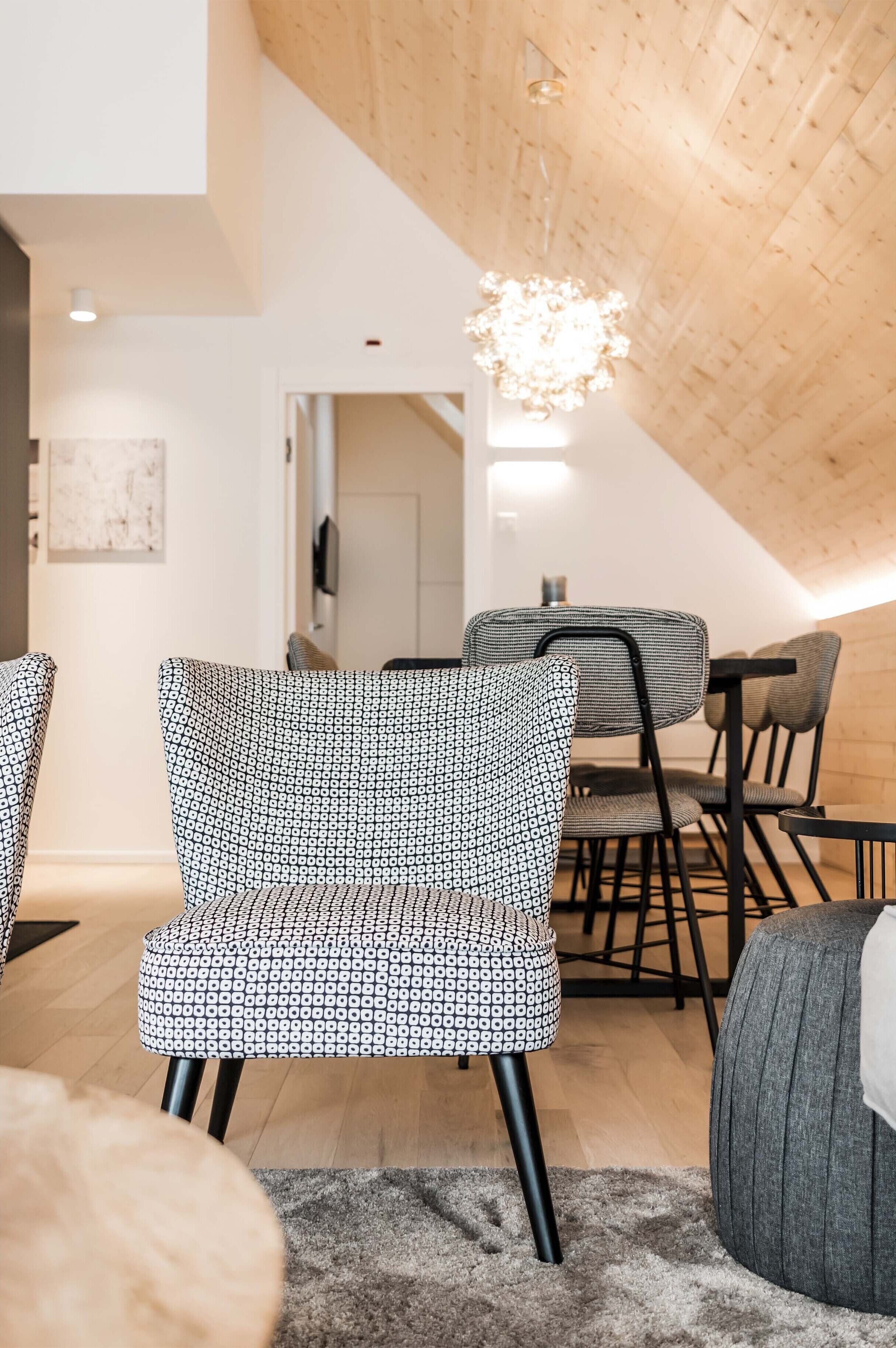 A modern interior with a high ceiling, patterned chairs, a dining table, and a chandelier.