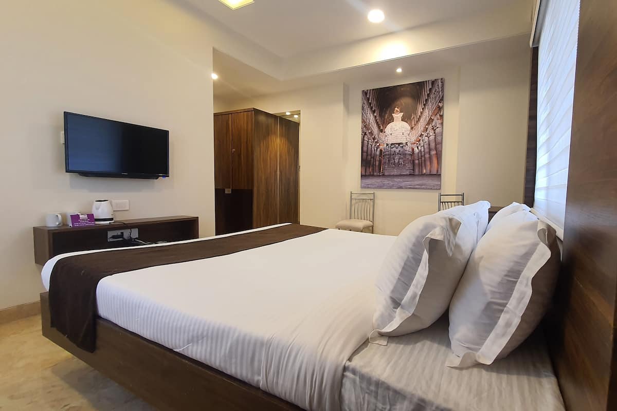 Une chambre d’hôtel avec un grand lit, un téléviseur à écran plat, une armoire en bois, une chaise et un tableau accroché au mur.