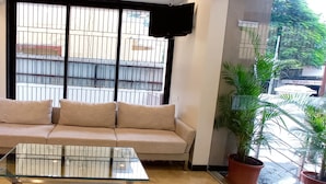 A living room with a beige sofa, a glass coffee table, and a large window with metal bars. - Purplebeds by VITS Aurangabad (Chhatrapati Sambhajinagar)