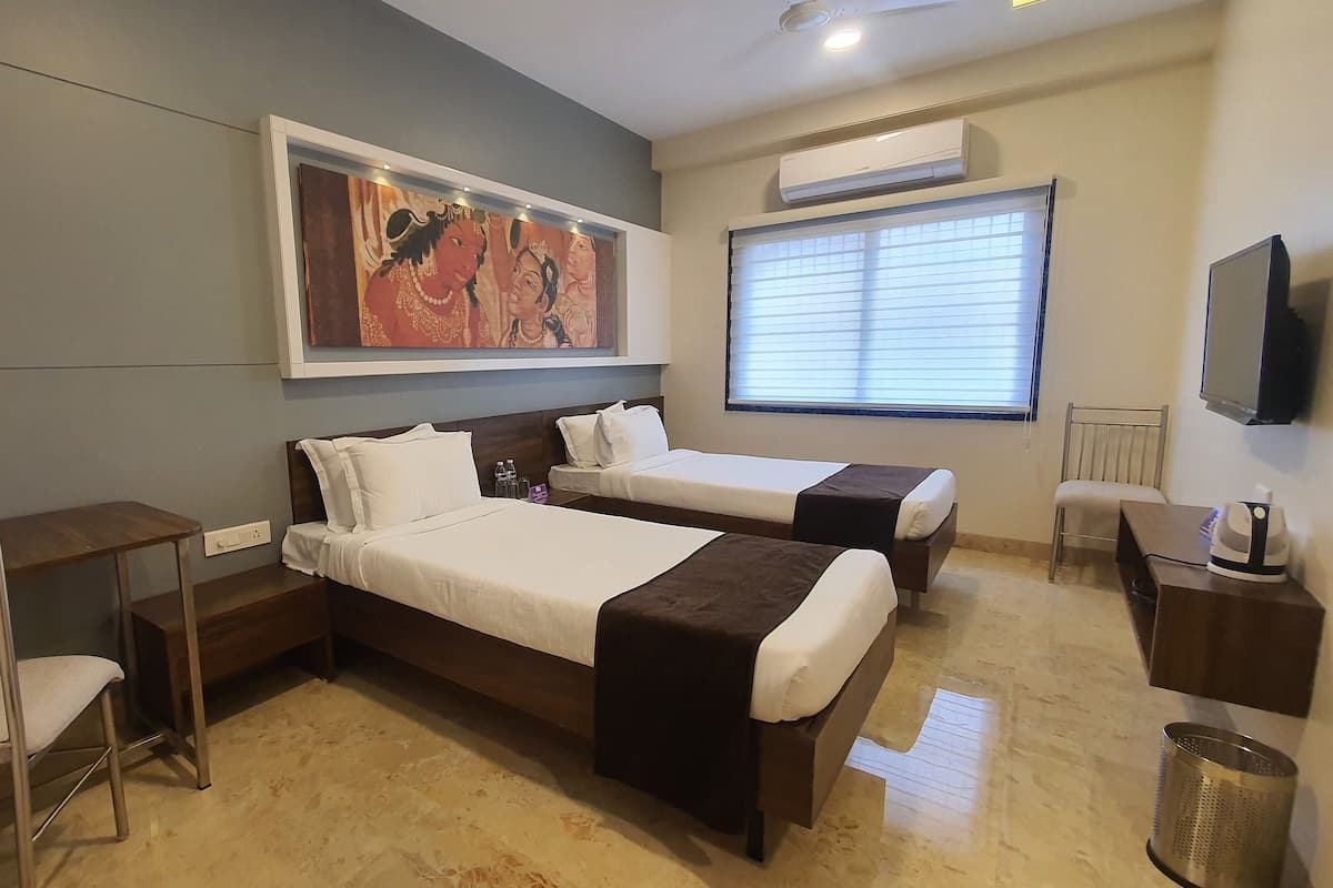Une chambre d’hôtel avec deux lits, un bureau, une chaise, une télévision et une fenêtre avec des stores.