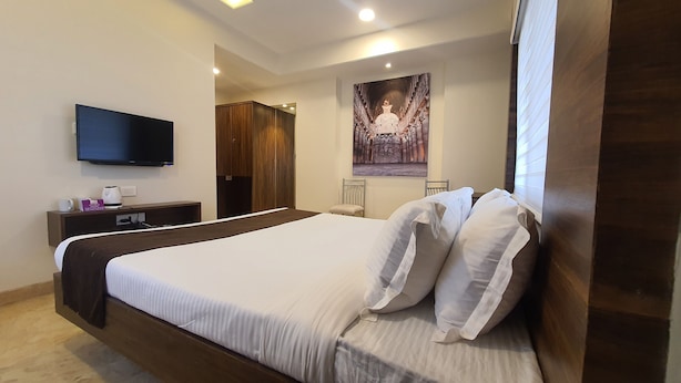 A hotel room with a large bed, a flat-screen TV mounted on the wall, a wooden wardrobe, and a poster on the wall. - Purplebeds by VITS Aurangabad (Chhatrapati Sambhajinagar)