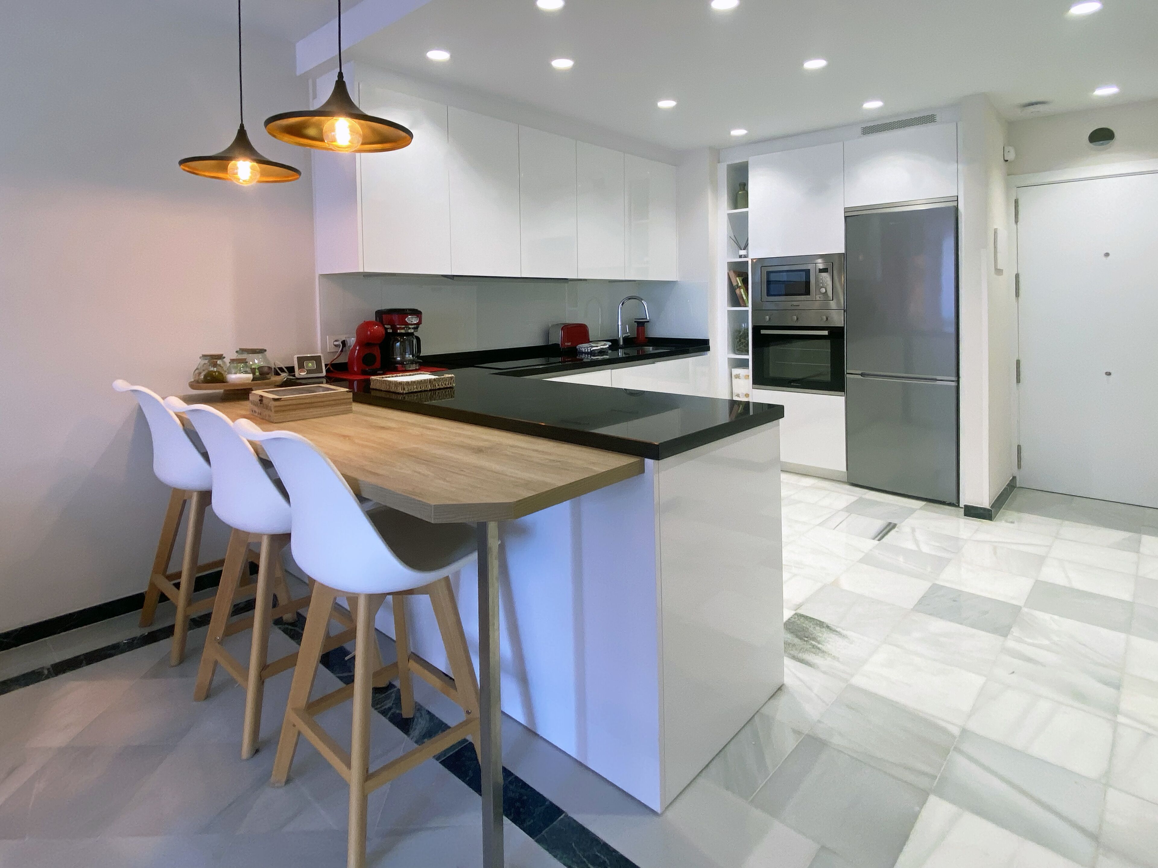Een moderne keuken met een centraal eiland, witte barkrukken, een koffieapparaat en roestvrijstalen apparatuur.