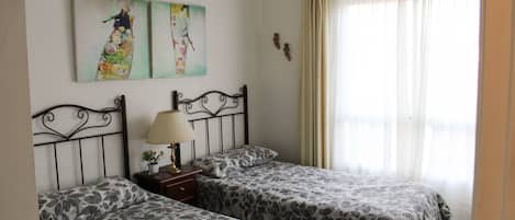 A room with two beds, a nightstand with a lamp, and two wall-mounted paintings.