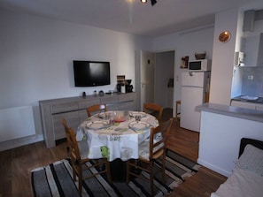 A compact living space with a dining area, kitchenette, and a TV mounted on the wall.