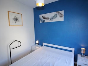 A bedroom with a white bed, a nightstand with a lamp, a framed picture on the wall, and a blue accent wall.