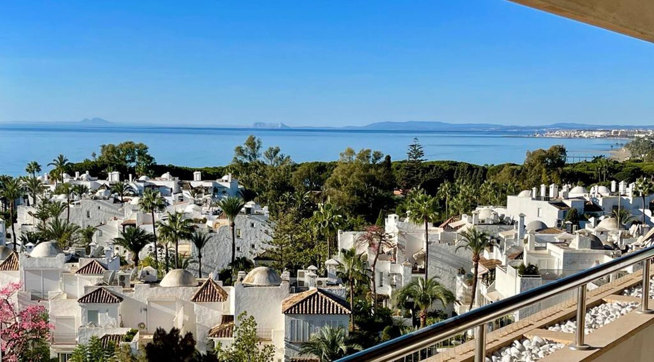 A coastal town with white buildings, palm trees, and a clear view of the sea.