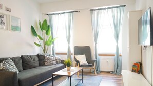 Een woonkamer met een bank, een fauteuil, een salontafel, een plant en een televisie.