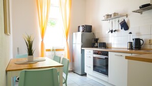 Een moderne keuken met een eethoek, met een koelkast, oven, koffiezetapparaat en een plant op de tafel.