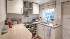 A compact kitchen with a gas stove, a sink, and a window with a view. - Charming Georgian flint cottage (BURY ST. EDMUNDS)