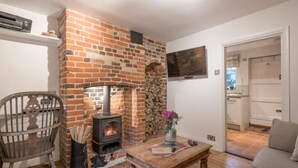 A living room with a brick fireplace, a wooden table, a chair, and a sofa. - Charming Georgian flint cottage (BURY ST. EDMUNDS)