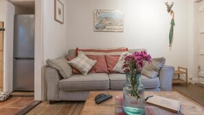 A living room with a grey sofa, a vase of flowers, a remote control, and a notebook on a wooden coffee table. - Charming Georgian flint cottage (BURY ST. EDMUNDS)