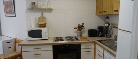 A compact kitchen with white cabinets, a microwave, a stove, a dishwasher, and a coffee maker.