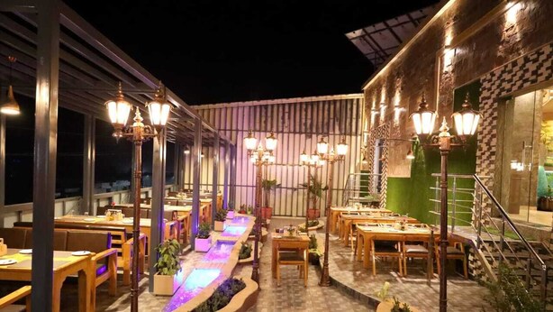 Un área de comedor al aire libre con mesas y sillas, una fuente de agua e iluminación decorativa.