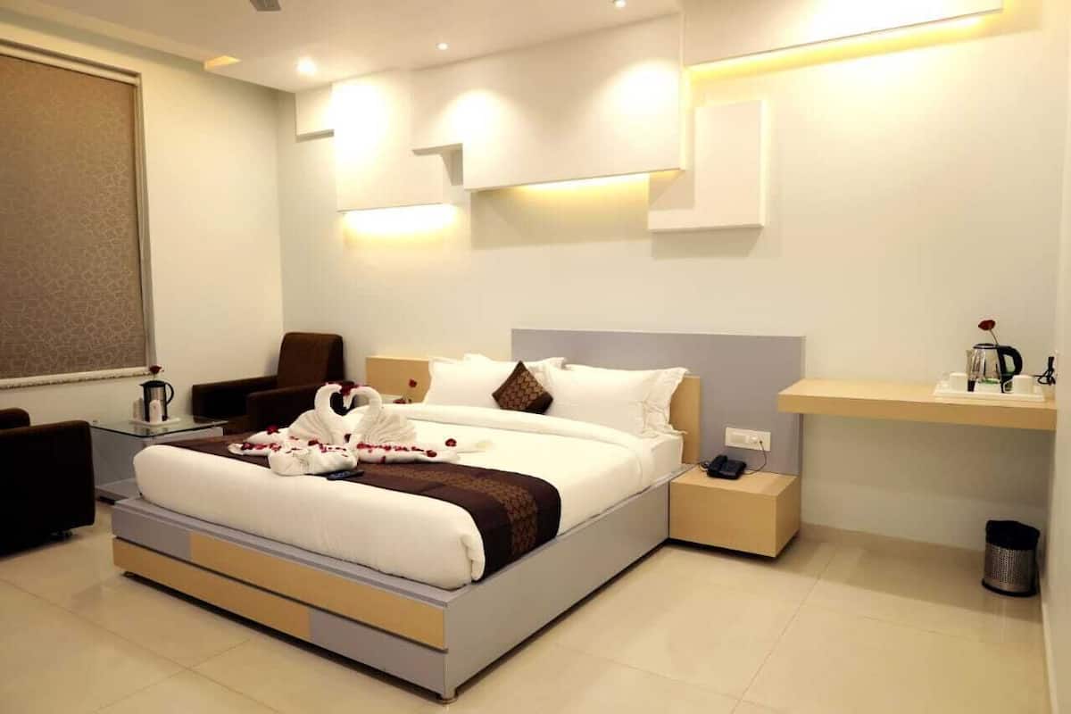 Quarto de hotel moderno com uma cama grande, mesas de cabeceira, escrivaninha e uma cadeira.