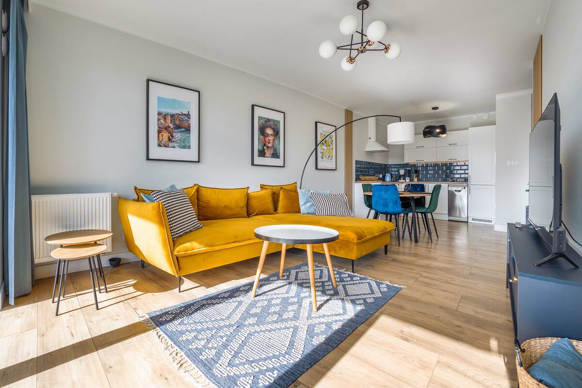 Una sala de estar moderna con un sofá amarillo, una mesita redonda y un tapete azul estampado.