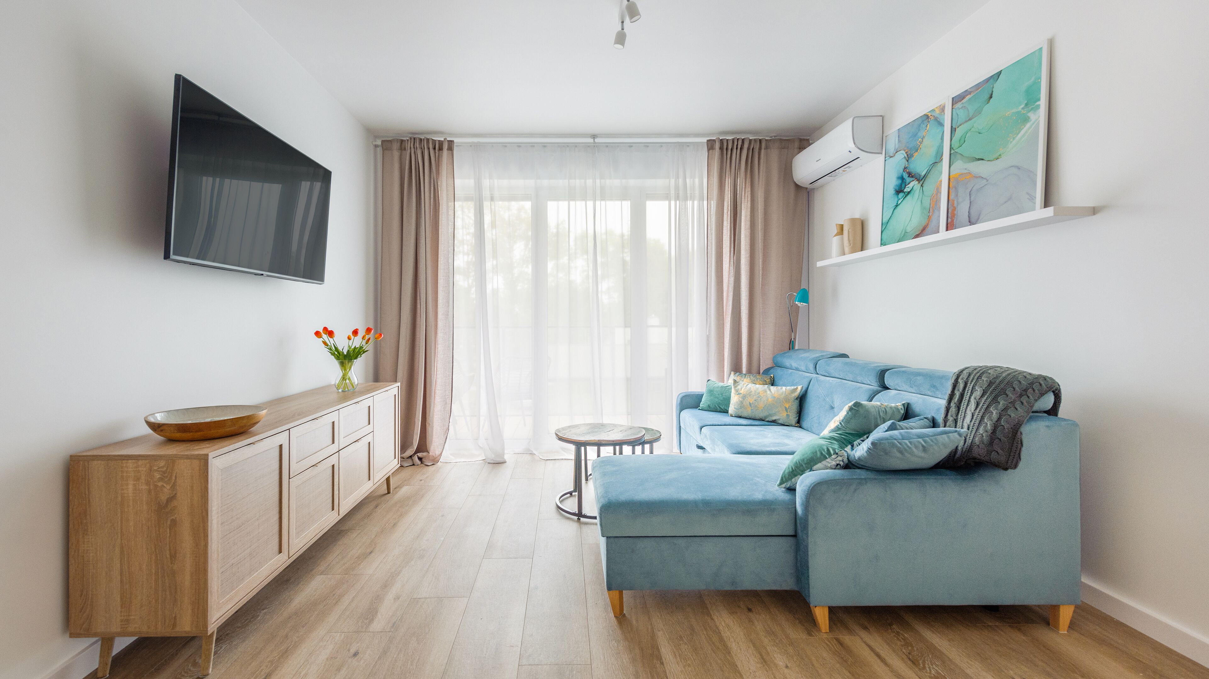 A modern living room with a blue sofa, wooden cabinet, and a flat-screen TV.