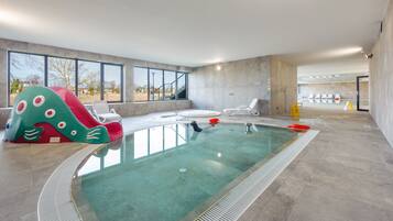 Piscina interna com um escorregador colorido, cadeiras de sol e vista para o exterior.