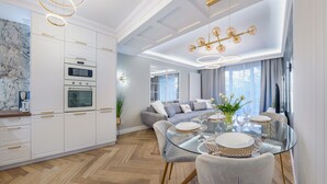 Cozinha moderna com eletrodomésticos embutidos, sala de jantar com mesa de vidro e sala de estar com sofá e cortinas.
