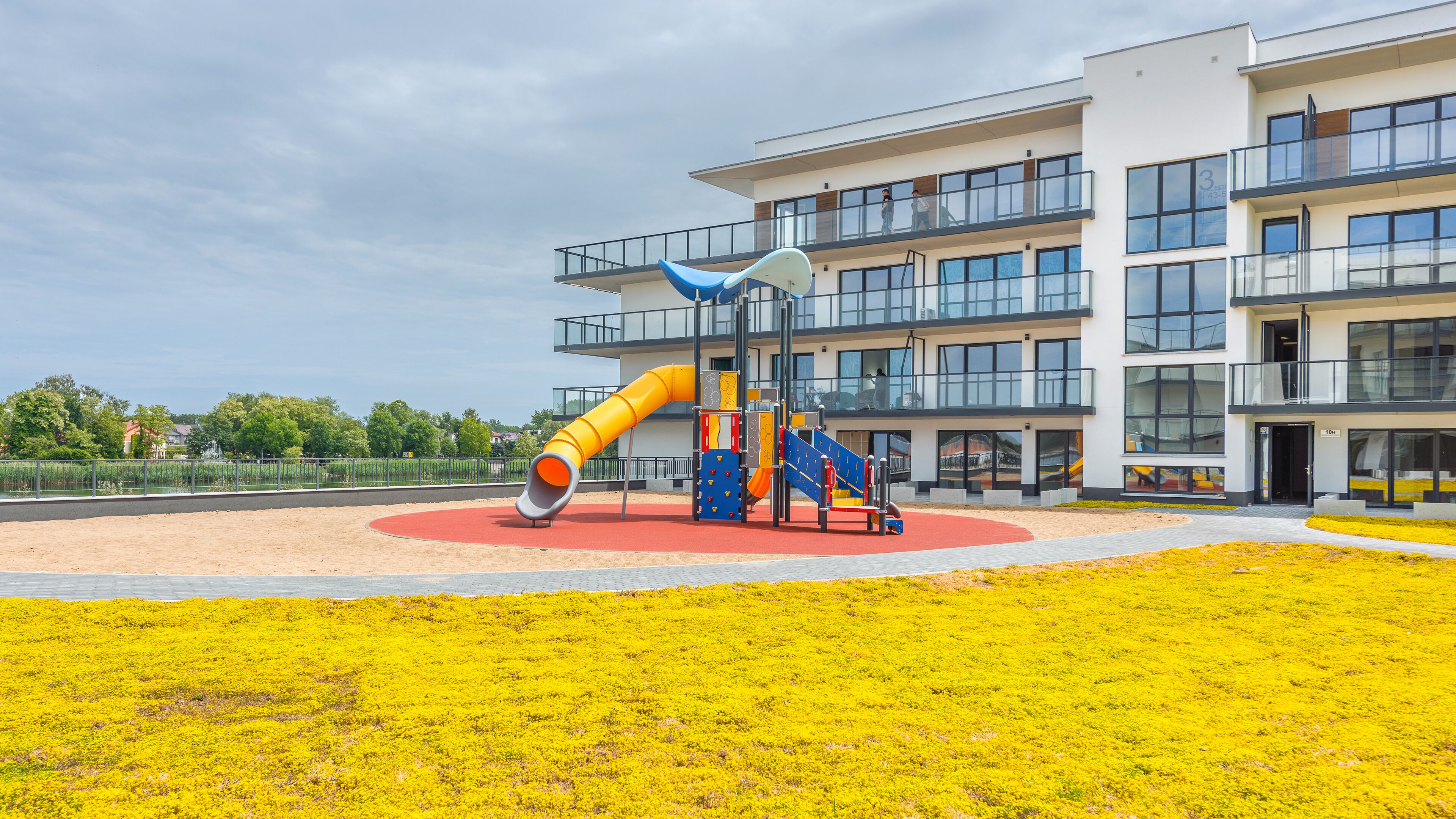 Un parque infantil con toboganes y estructuras de escalada frente a un edificio moderno con varios balcones.