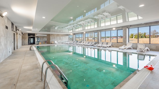 Piscina interior moderna com água cristalina, espreguiçadeiras e amplas janelas com vista para o exterior.
