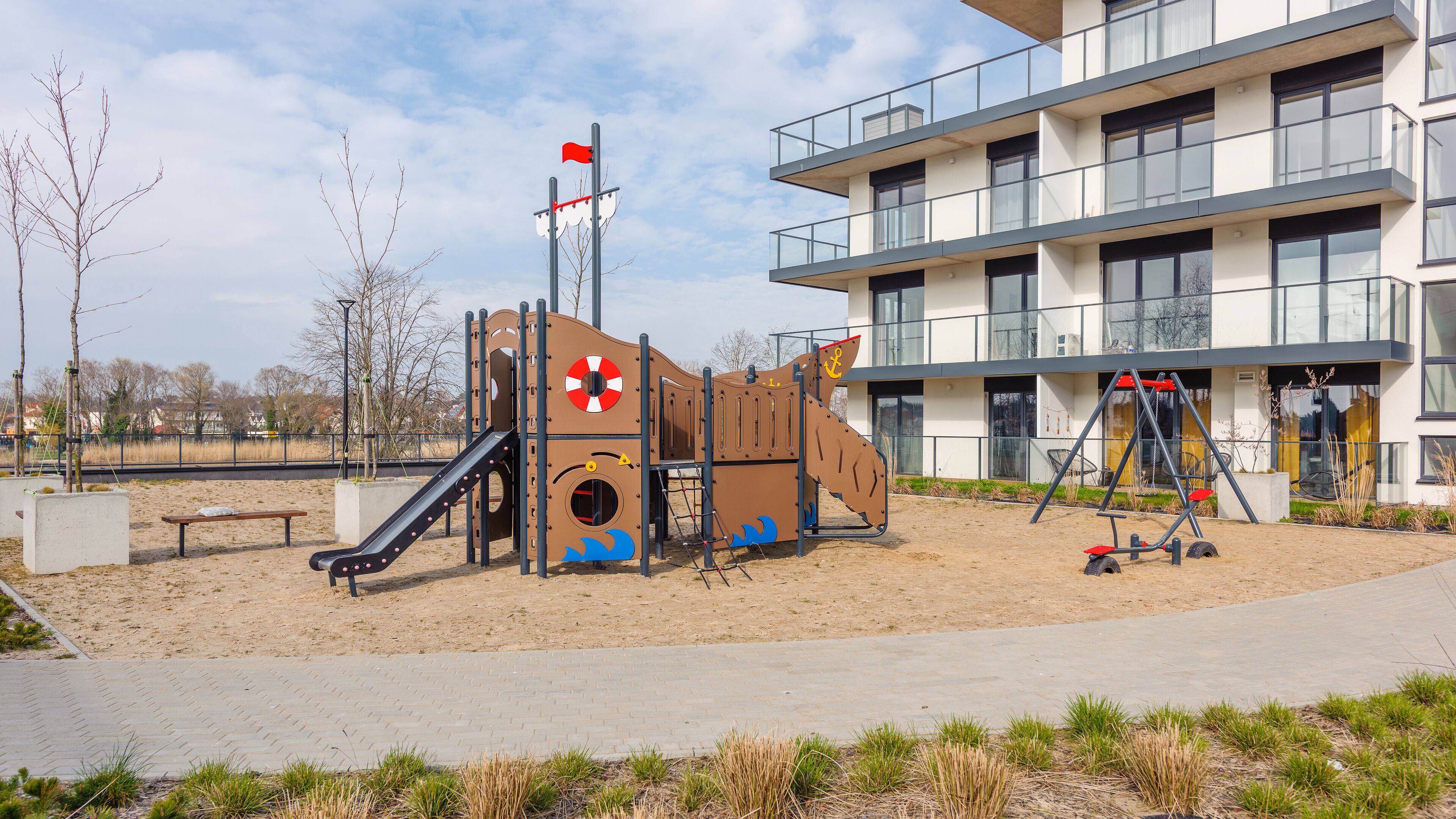A playground with a slide and climbing structures, adjacent to a modern building with balconies.