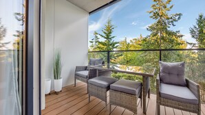Varanda com mobiliário de vime, mesa de vidro e vista para árvores.