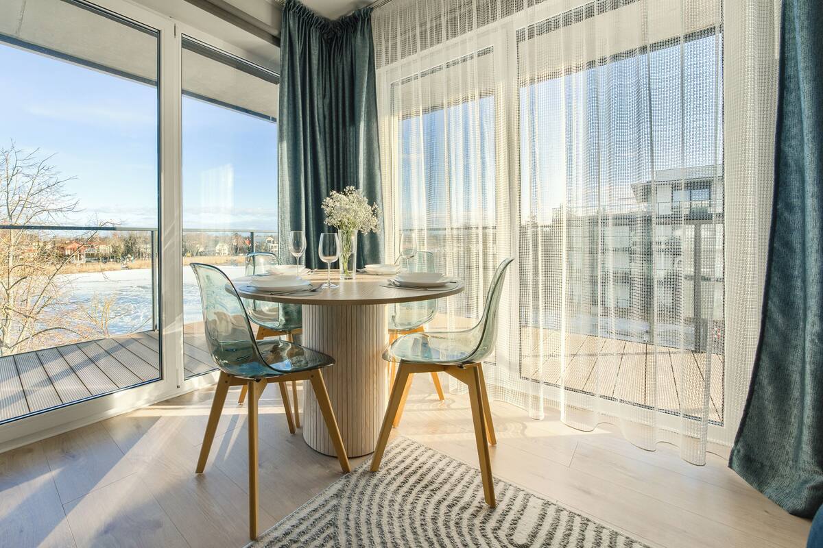 Un comedor moderno con una mesa redonda, sillas transparentes y vistas a un paisaje nevado a través de amplias ventanas.