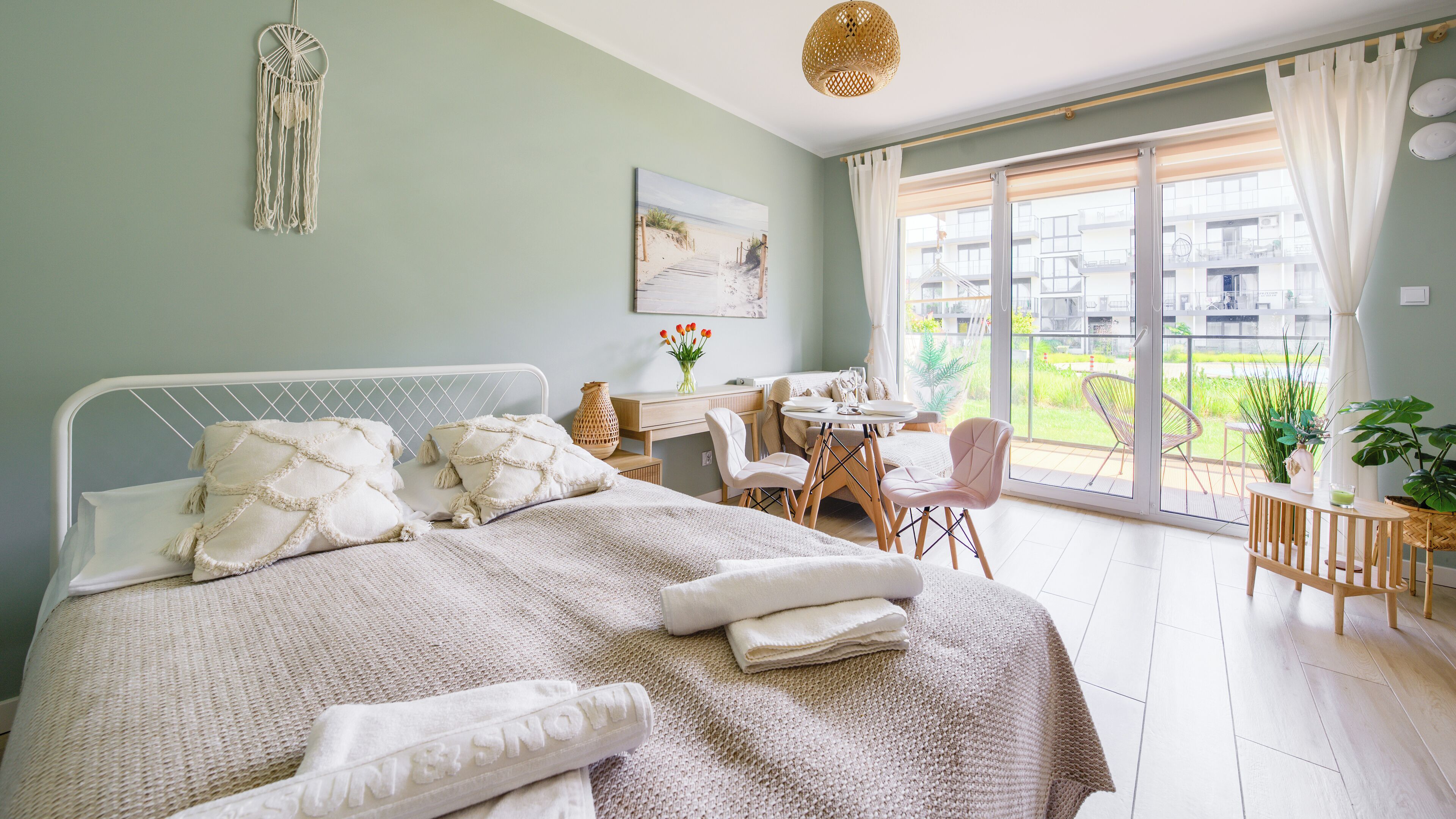 A bedroom with a bed, a desk, and a view of a balcony.