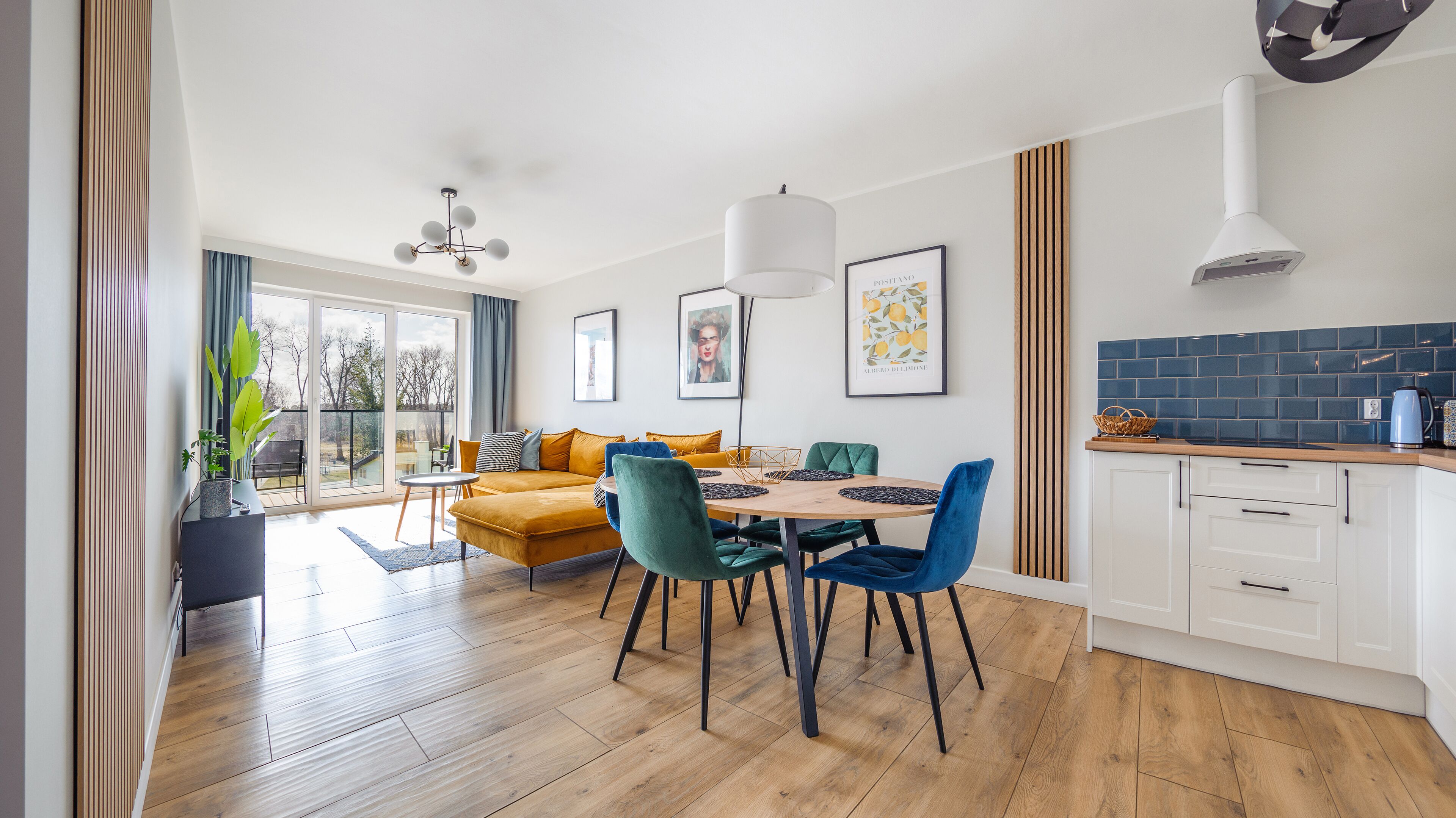 A modern living room with a sofa, chairs, and a dining table. There is a kitchen area with cabinets and a stove.