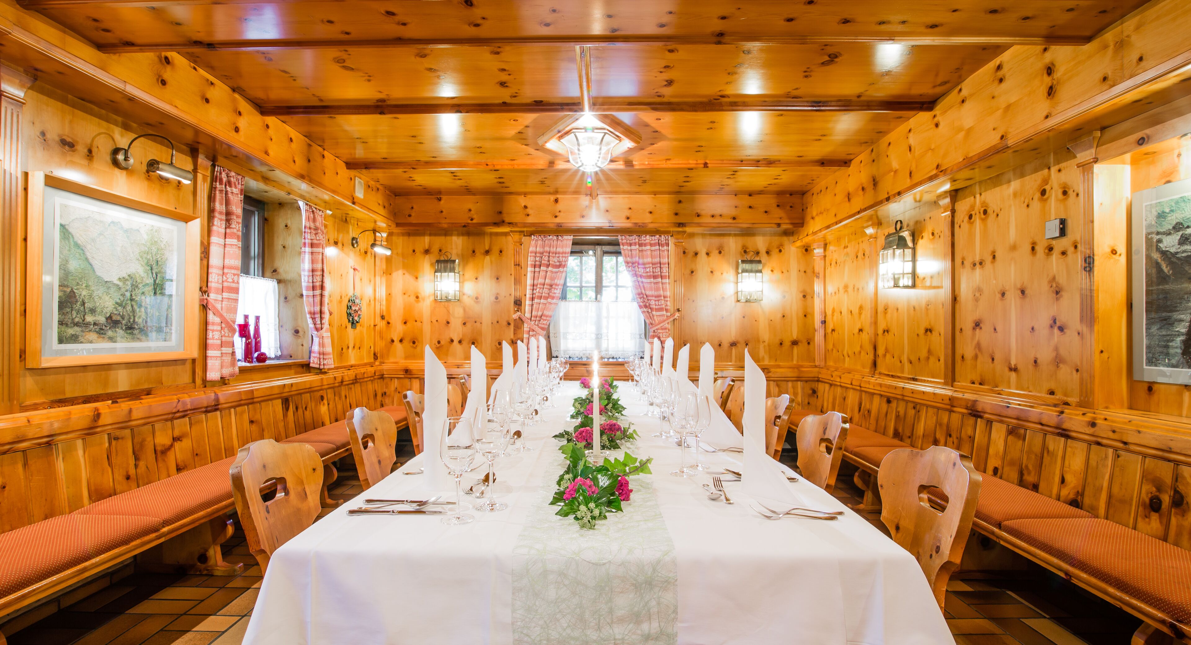 Una larga mesa de comedor con mantel blanco y centros de mesa florales, rodeada de sillas de madera.