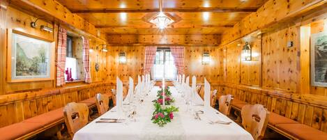 Una larga mesa de comedor con mantel blanco y centros de mesa florales, rodeada de sillas de madera.