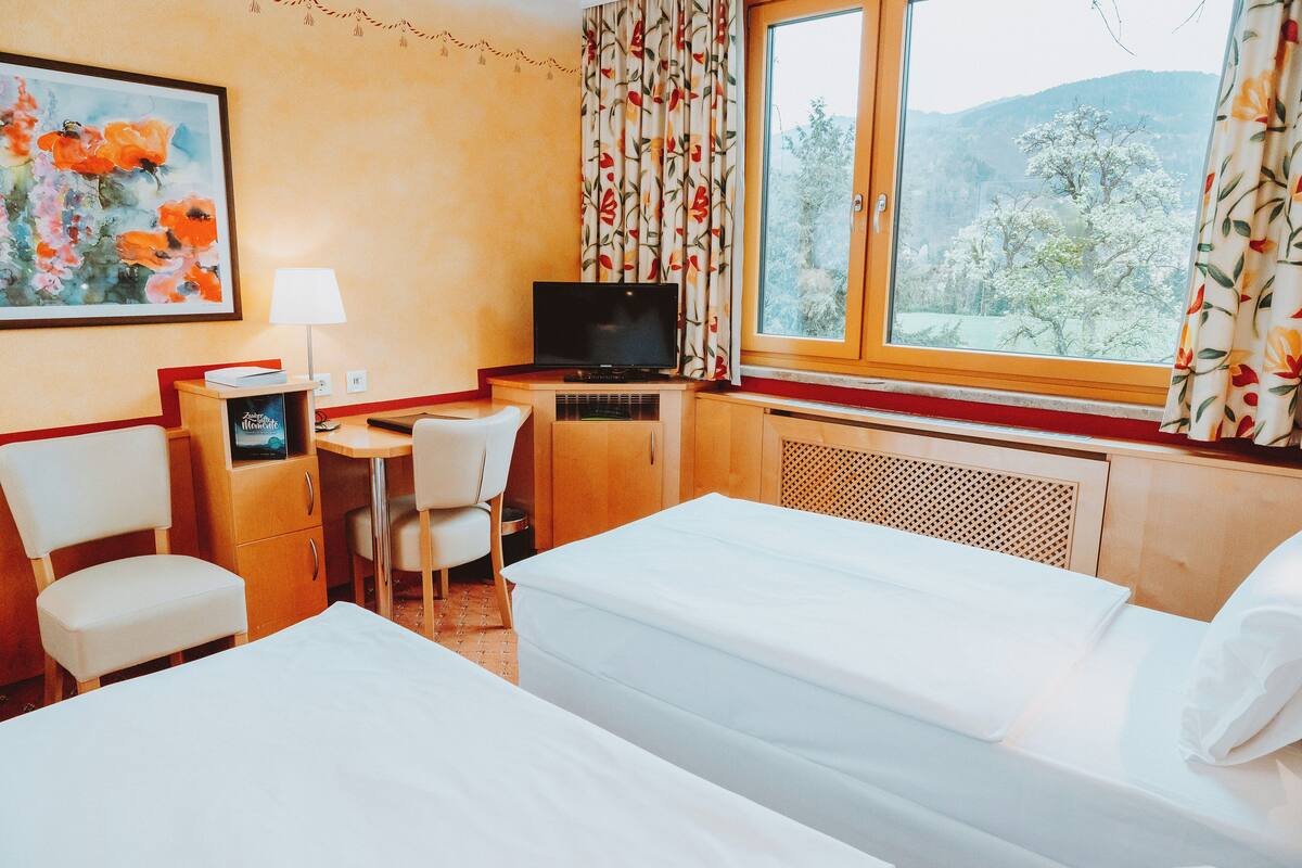 Ein Hotelzimmer mit Bett, Schreibtisch mit Fernseher, einem Sessel und einem Fenster mit Vorhängen.