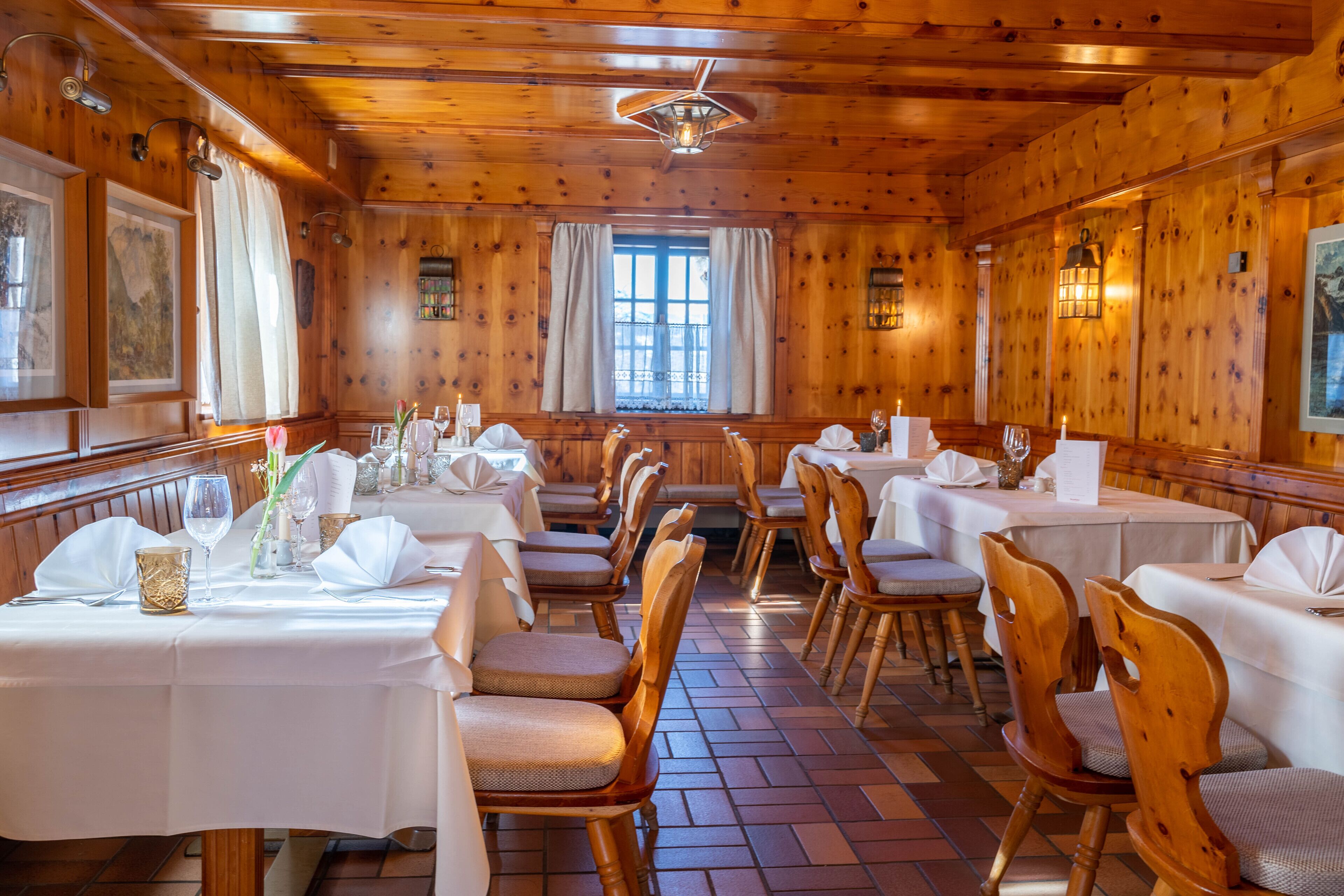 A restaurant with wooden walls and ceiling, white tablecloths, and wooden chairs.
