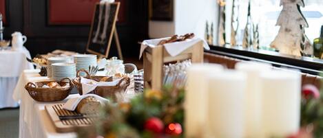 Una mesa de comedor dispuesta con platos, cestas y velas, con un árbol de Navidad y adornos al fondo.
