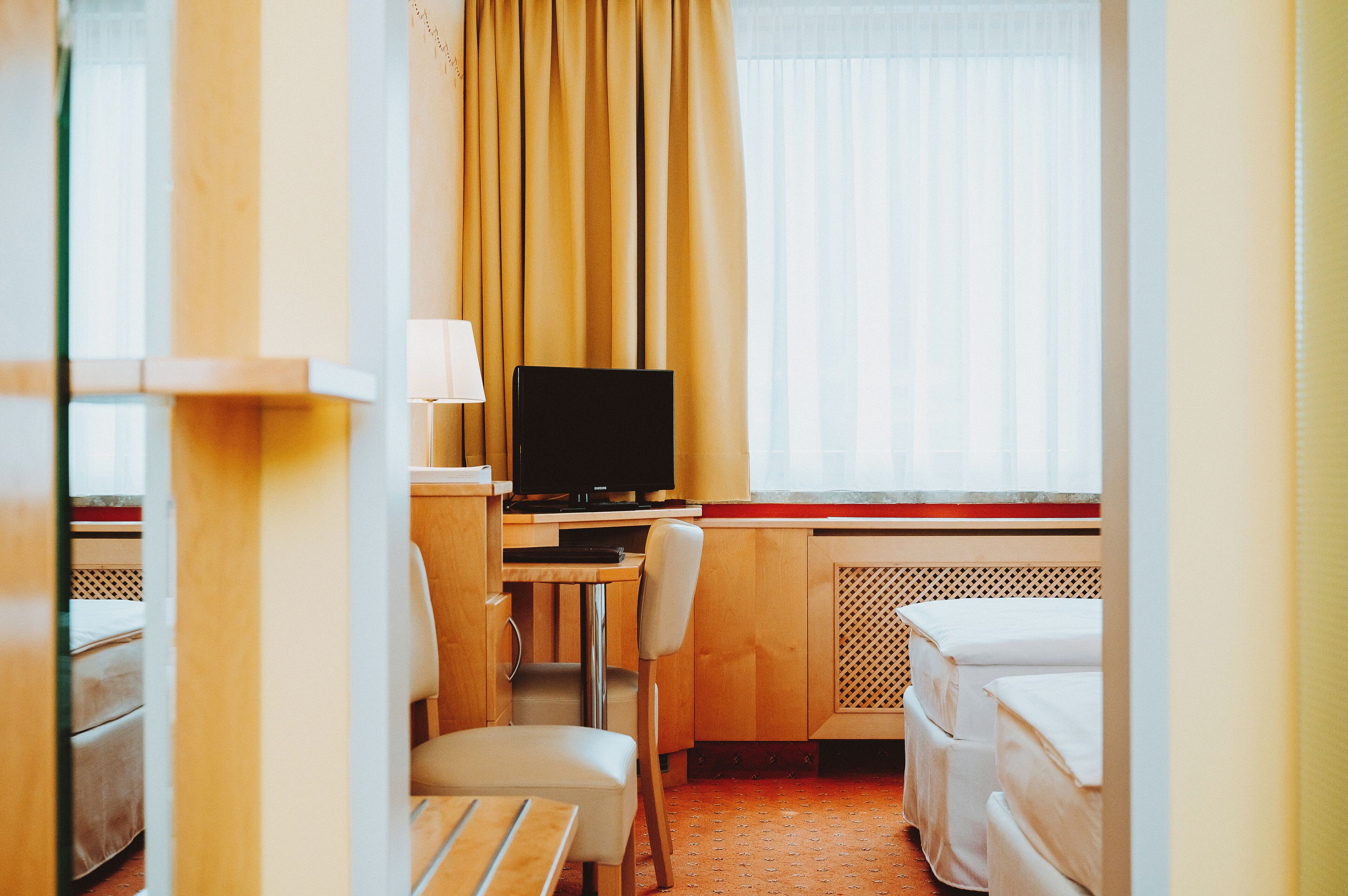A hotel room with a bed, a desk with a computer, a chair, and a window with curtains.