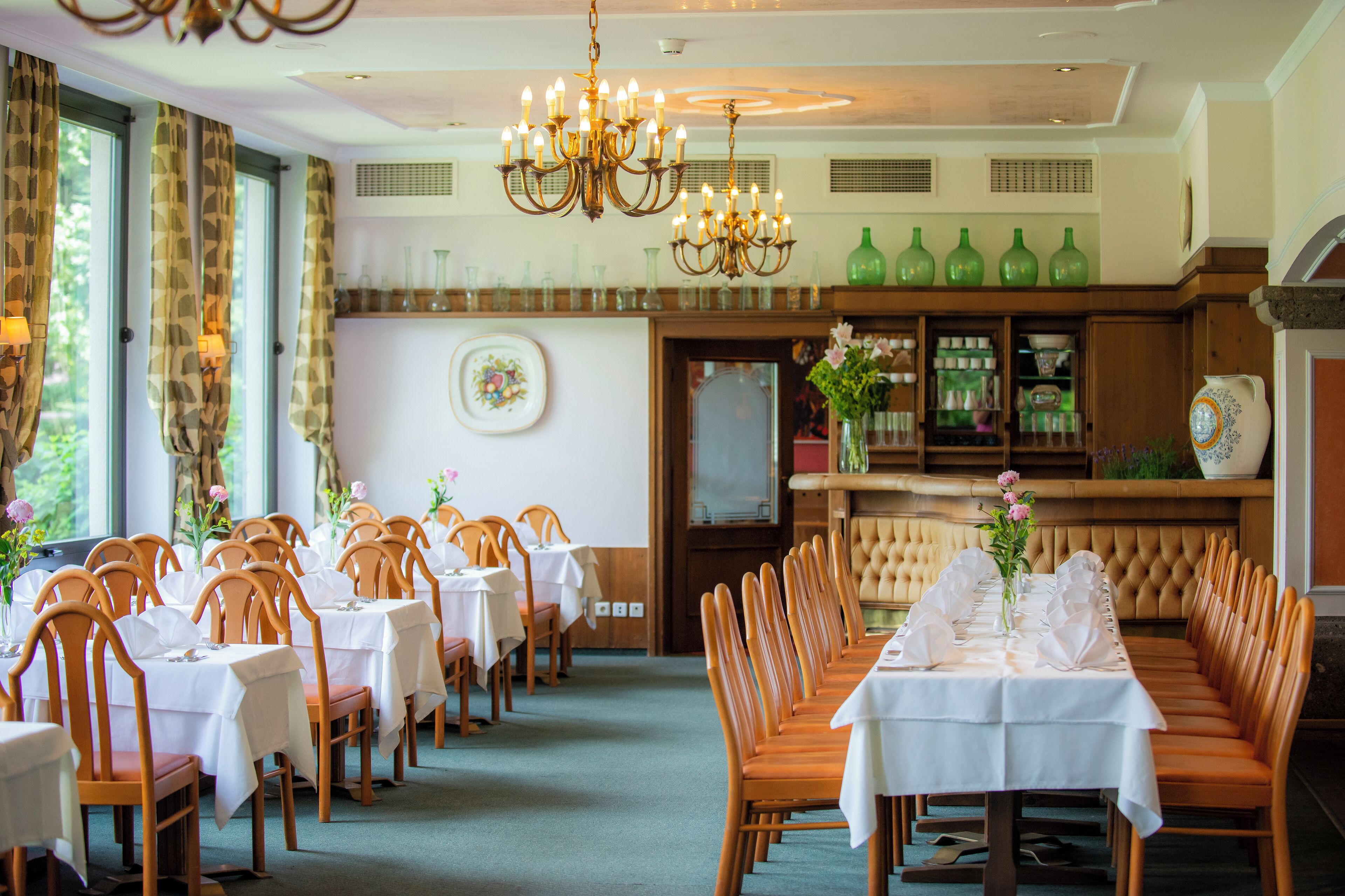 Uma sala de jantar formal com várias mesas e cadeiras, um candelabro e um espaço de bar com prateleiras.