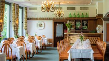 Uma sala de jantar formal com várias mesas e cadeiras, um candelabro e um espaço de bar com prateleiras.
