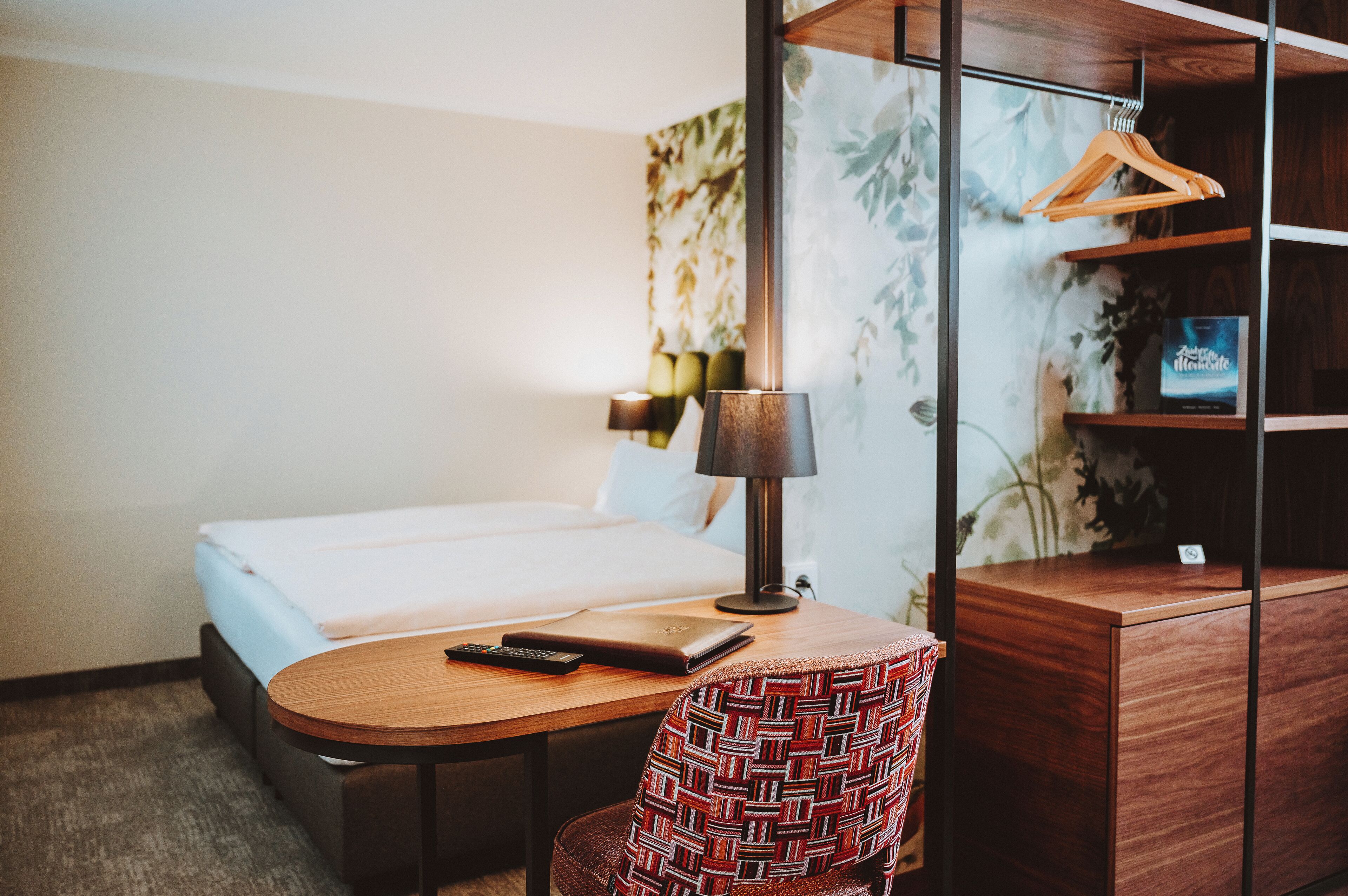 Una habitación de hotel con cama, escritorio, laptop, silla, lámpara y armario.