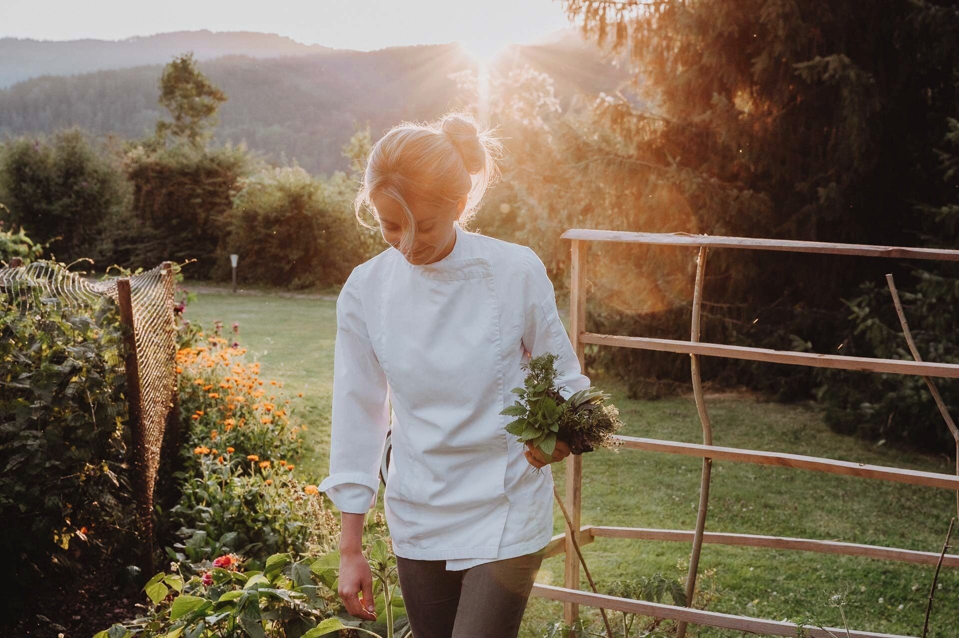 A person in a white shirt standing in a garden with a metal fence and greenery in the background.
