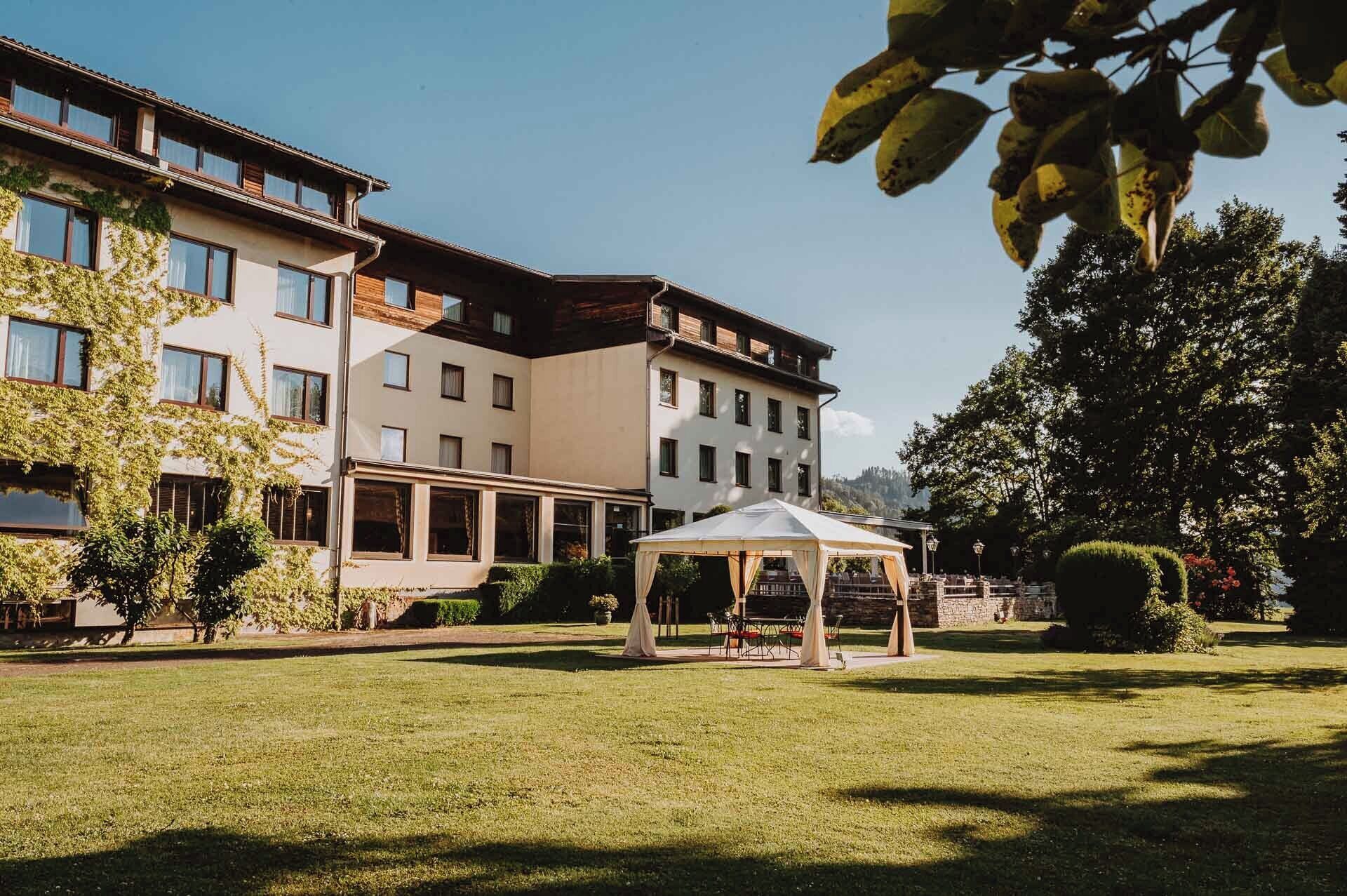 Ein Hotel mit überdachter Außenbereich-Sitzgelegenheit, einem gepflegten Rasen und einem großen Baum.